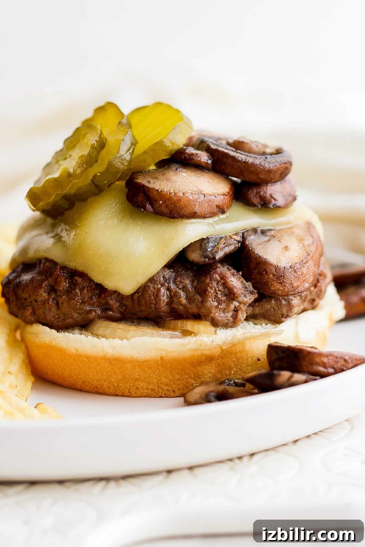 Grilled Mushroom Swiss Burger Recipe 8 a burger with mushrooms and pickles on a plate.