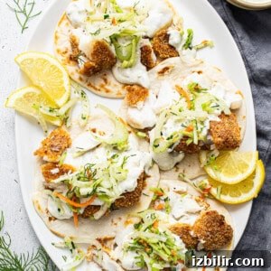 Fish tacos on a white plate with lemon wedges.