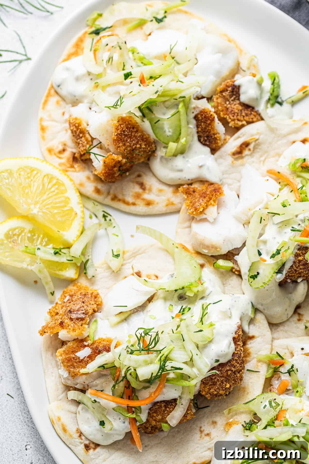 Fish tacos with slaw and lemon wedges on a white plate.