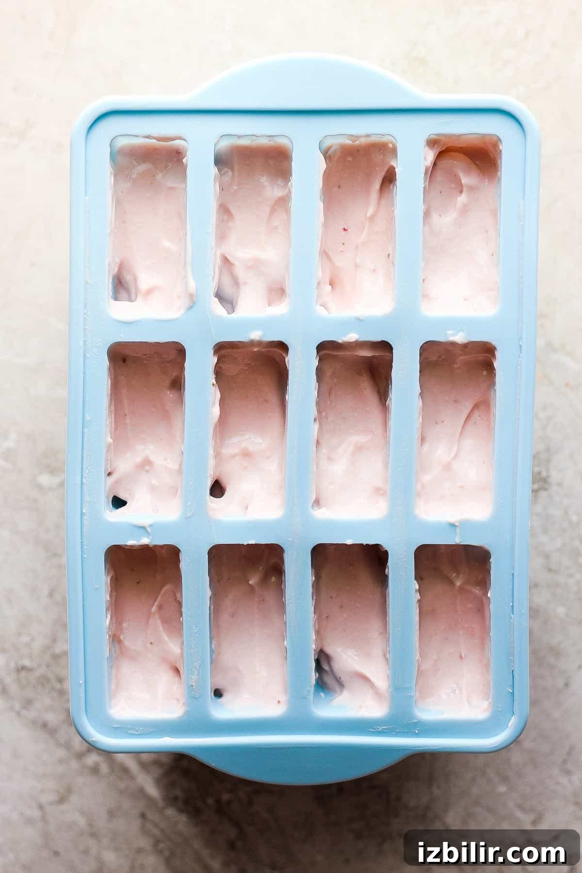 A blue ice cube tray filled with pink ice cream.