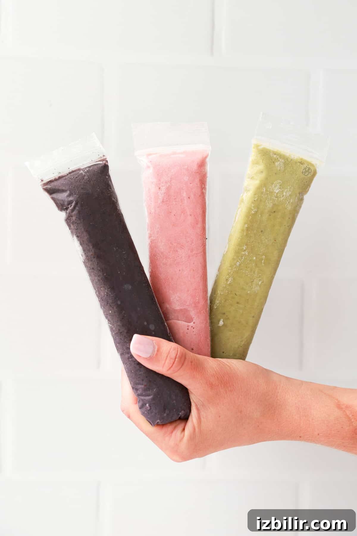 A hand holding three frozen popsicles.