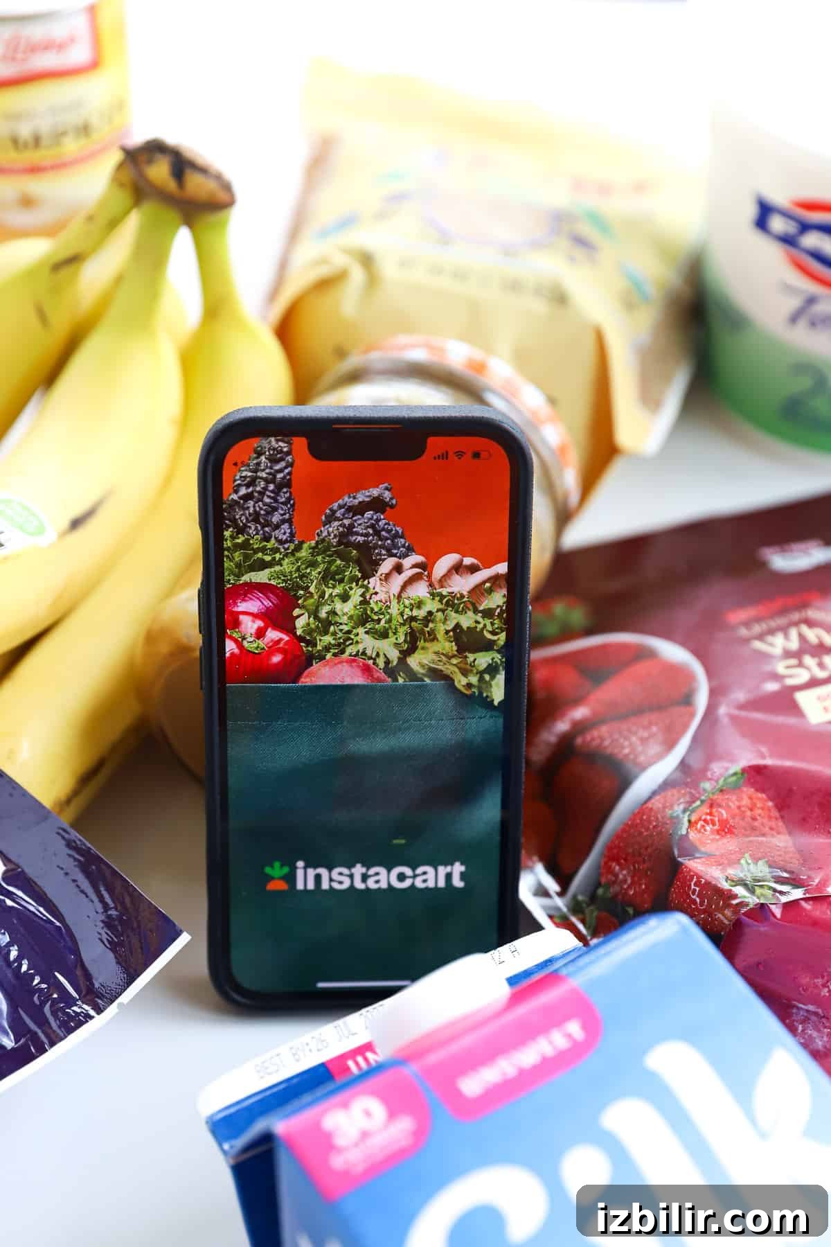A mobile phone sits on a table next to a pile of fruit and vegetables.