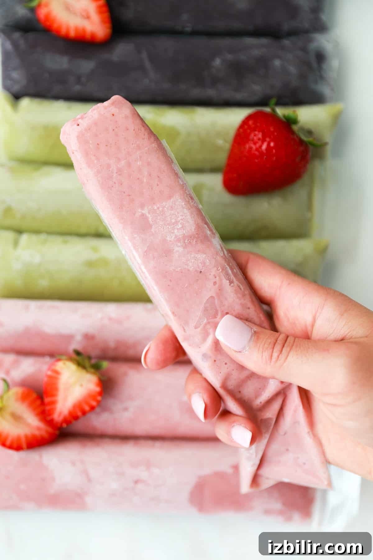 A person holding a strawberry popsicle in front of a pile of strawberries.
