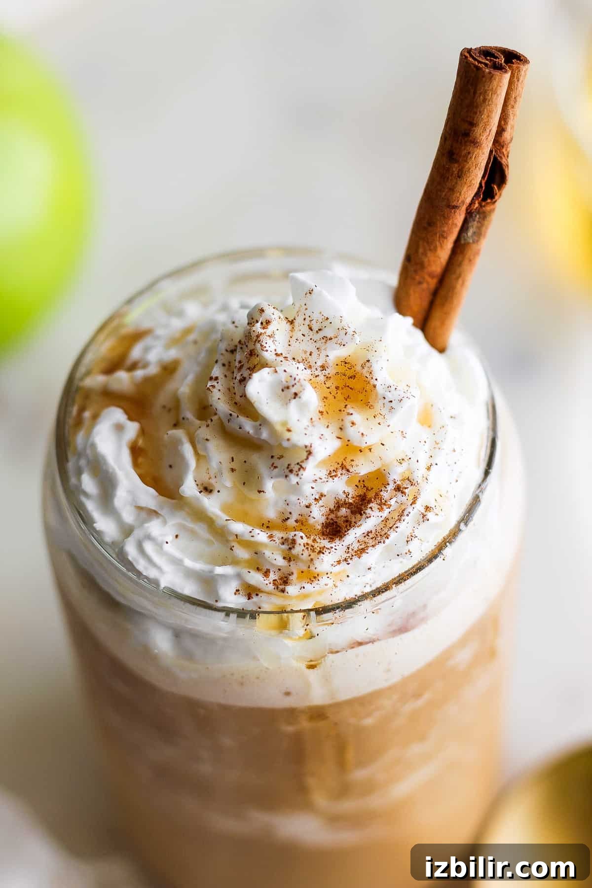 An apple latte with whipped cream and a cinnamon stick.