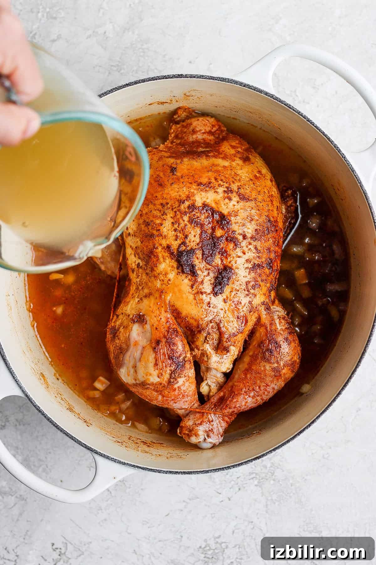 a person pouring liquid over a chicken in a pot.