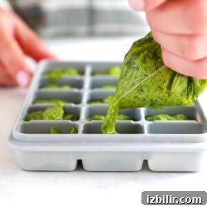 A person preparing homemade pesto by pouring it into an ice cube tray.