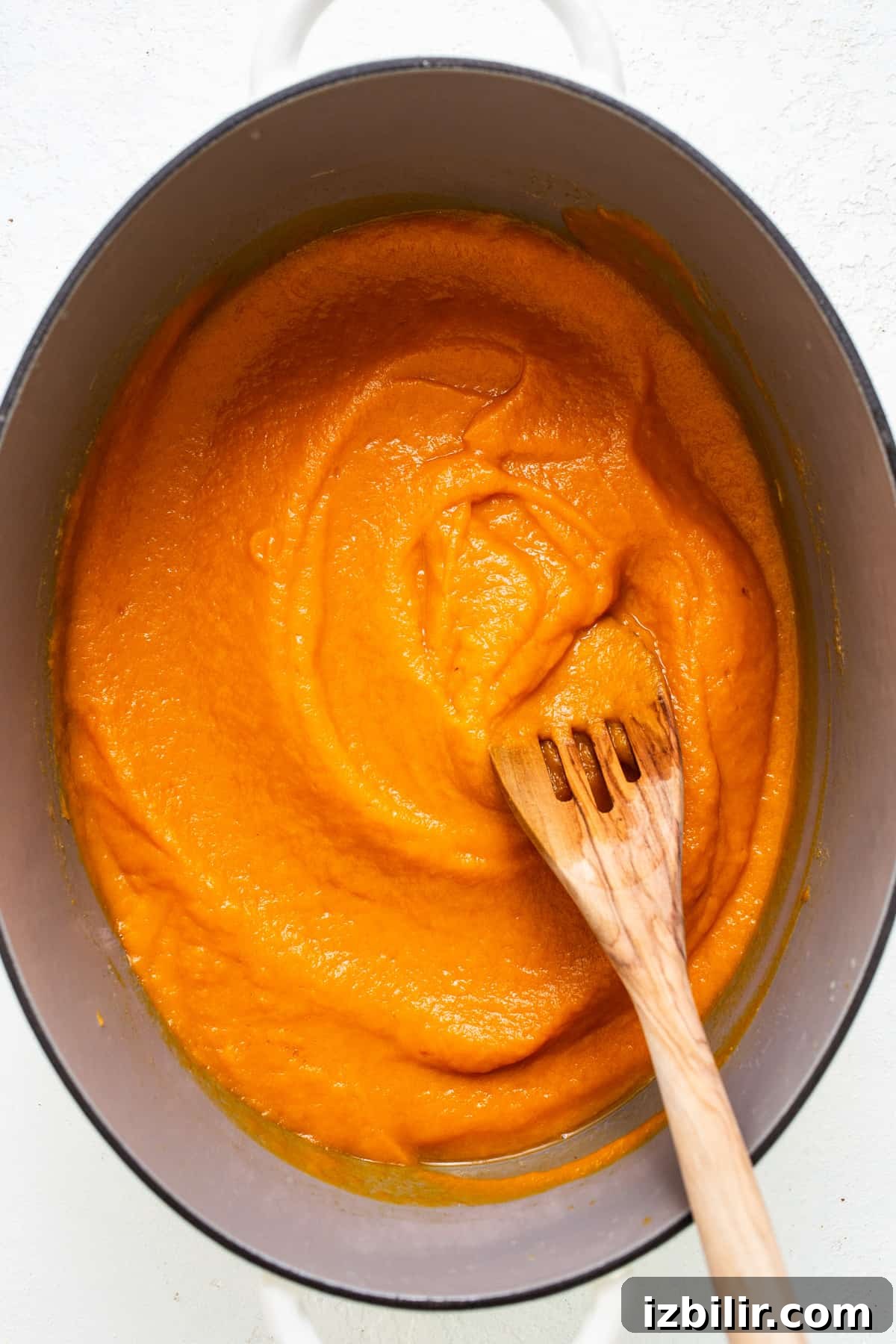 A wooden spoon in a pot of orange sauce.