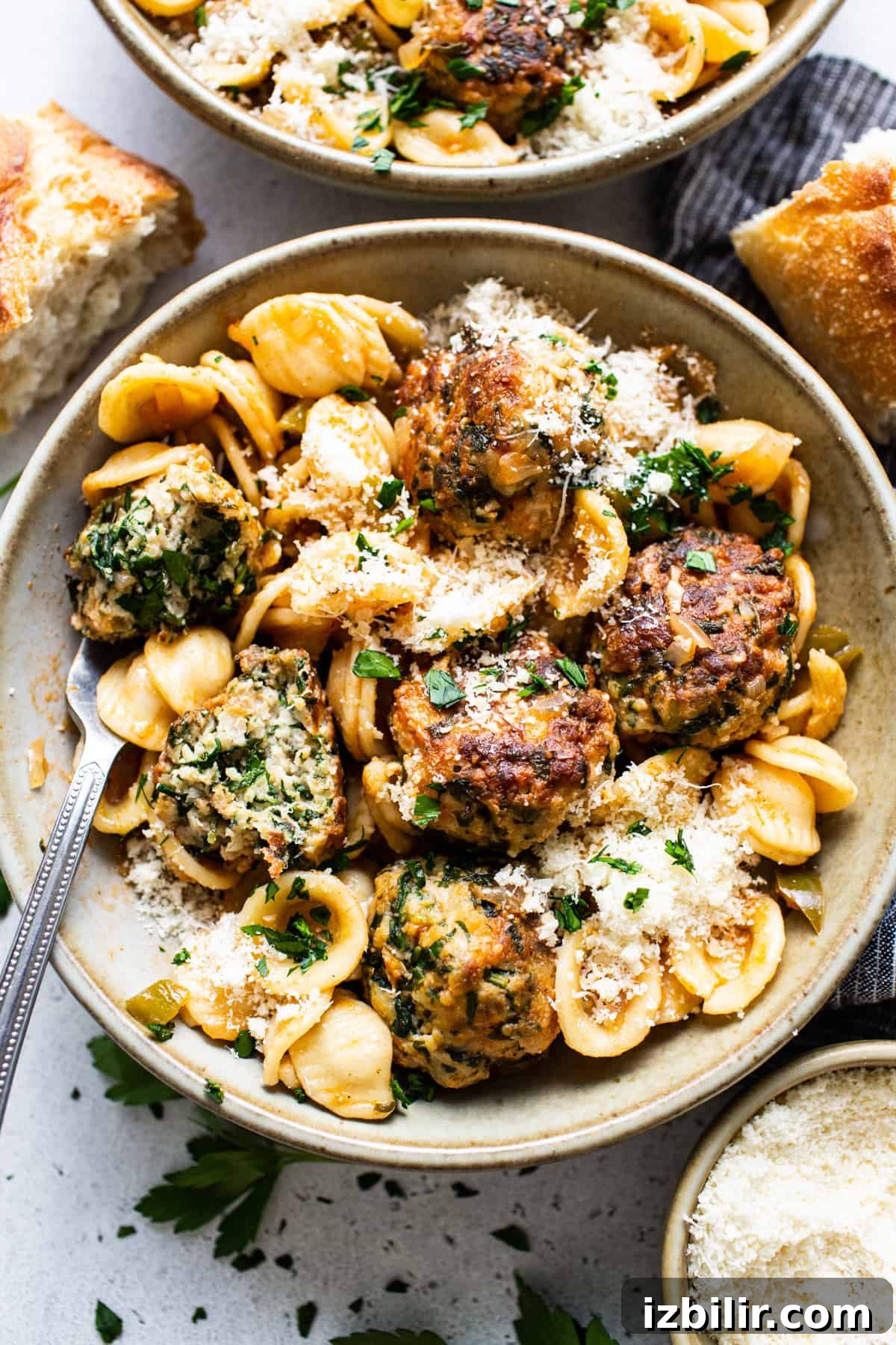 A bowl of pasta with meatballs and parmesan.