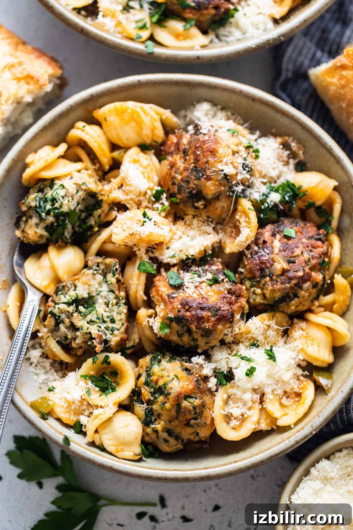A bowl of pasta with meatballs and parmesan.