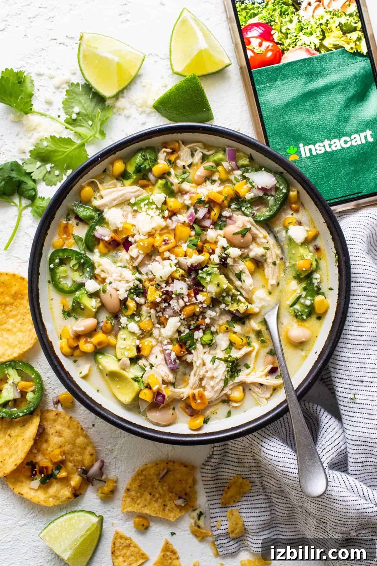 A bowl of chicken and corn soup with tortilla chips and limes.