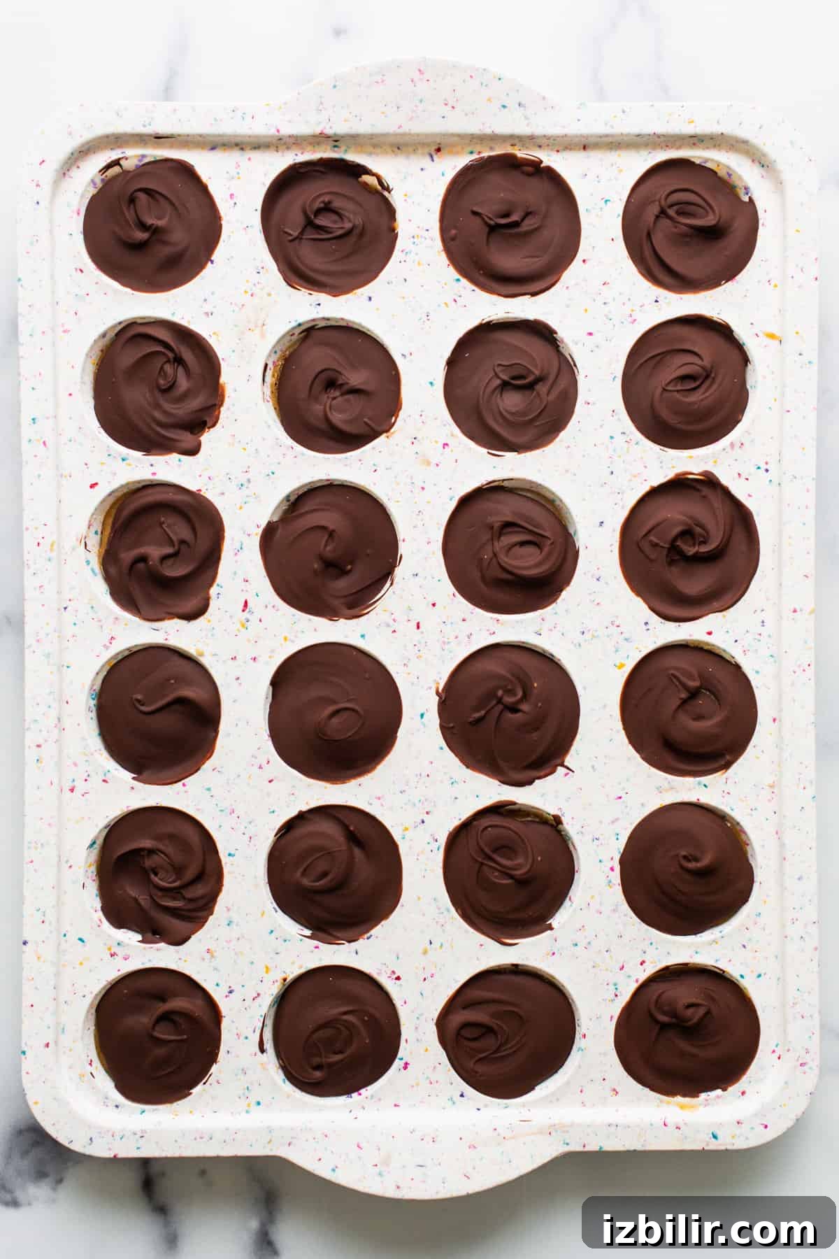 No-Bake Peanut Butter Twix Cups Recipe 5 A tray of chocolate dipped cupcakes on a marble countertop.
