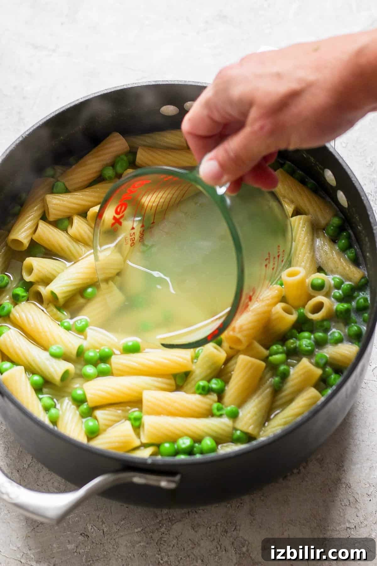 Creamy One-Pot Boursin Pasta Recipe 5 A person pouring pasta and peas into a pan.
