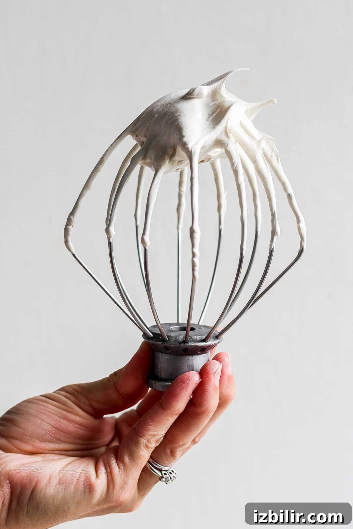 How to Make Brown Sugar Swiss Meringue 2 A person holding a whisk with whipped cream in it.