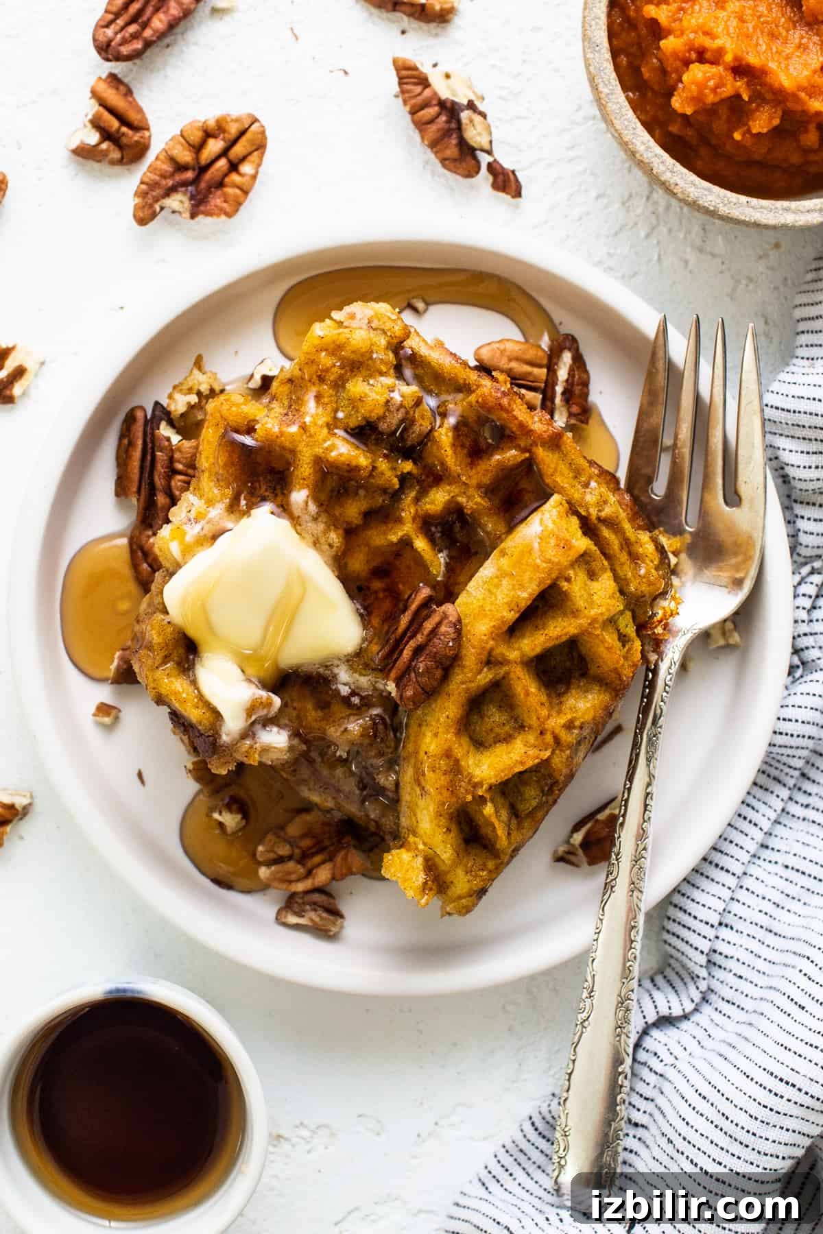 Pumpkin waffles with butter and pecans on a plate.