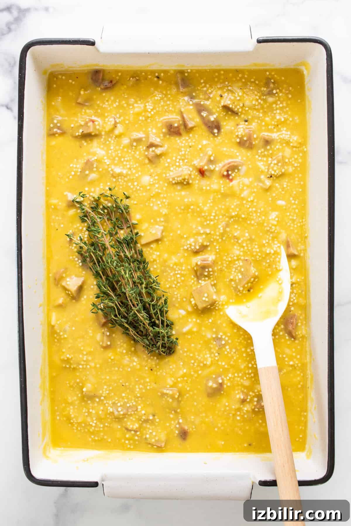 A bowl of soup with a spoon and a sprig of thyme.