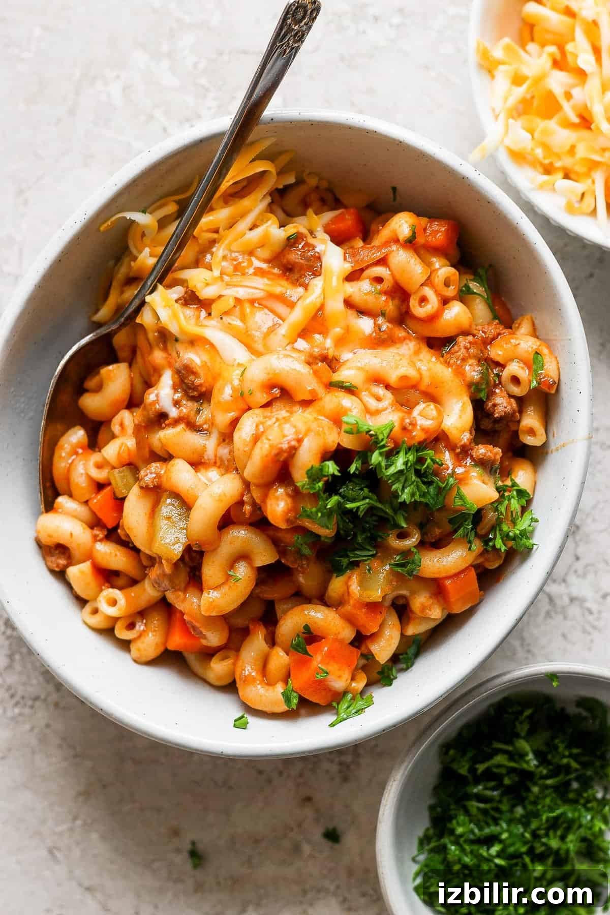A bowl of macaroni and cheese with meat and vegetables garnished with parsley.