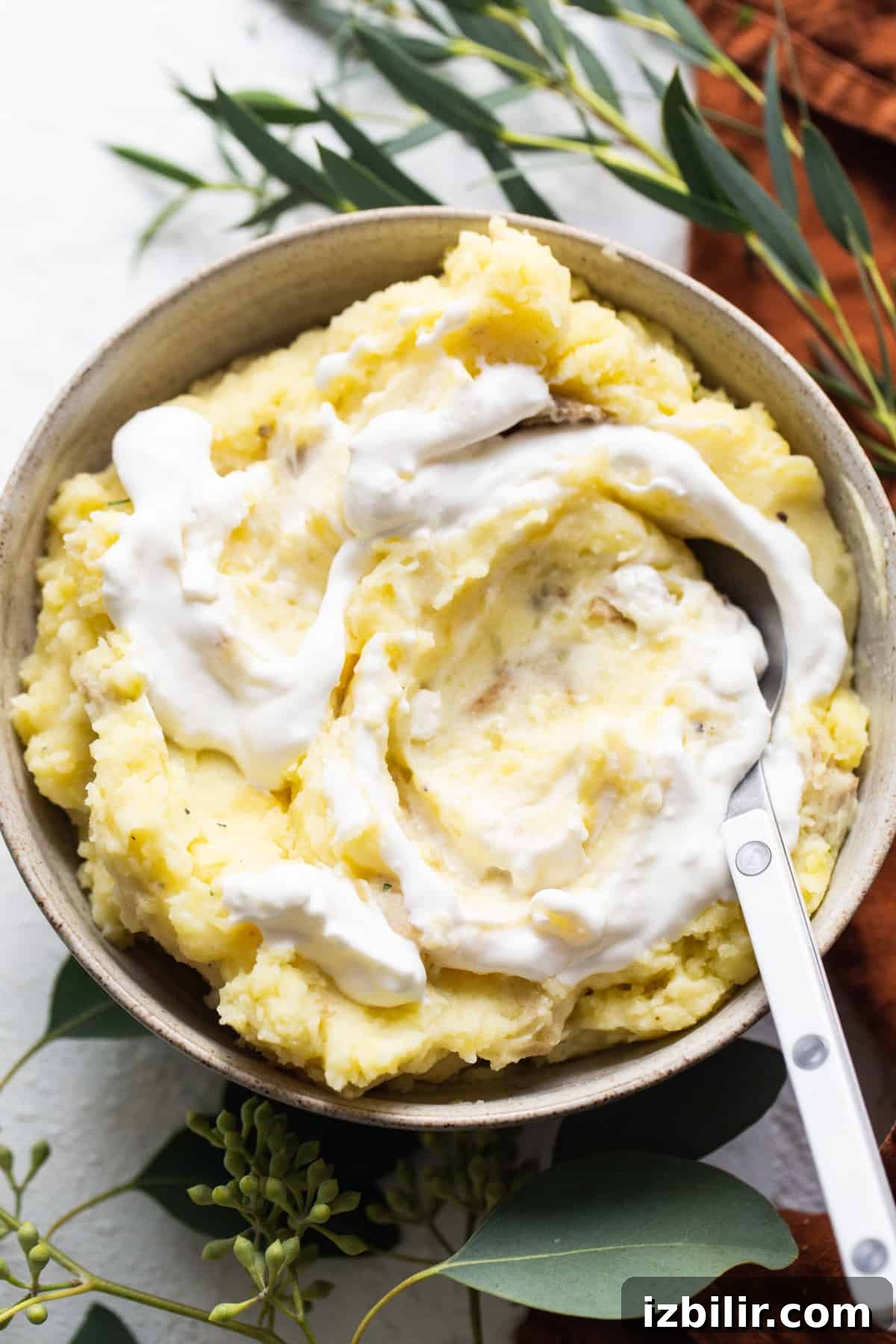 A bowl of mashed potatoes with whipped cream and eucalyptus leaves.