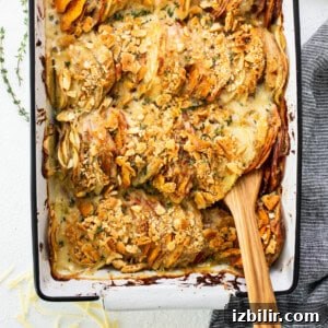 Classic Sweet Potato Au Gratin Recipe 7 A baking dish filled with roasted potatoes and a wooden spoon.