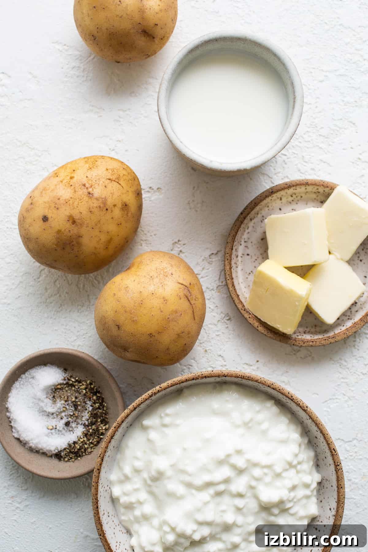 A bowl of potatoes, butter, salt and seasonings on a white background.