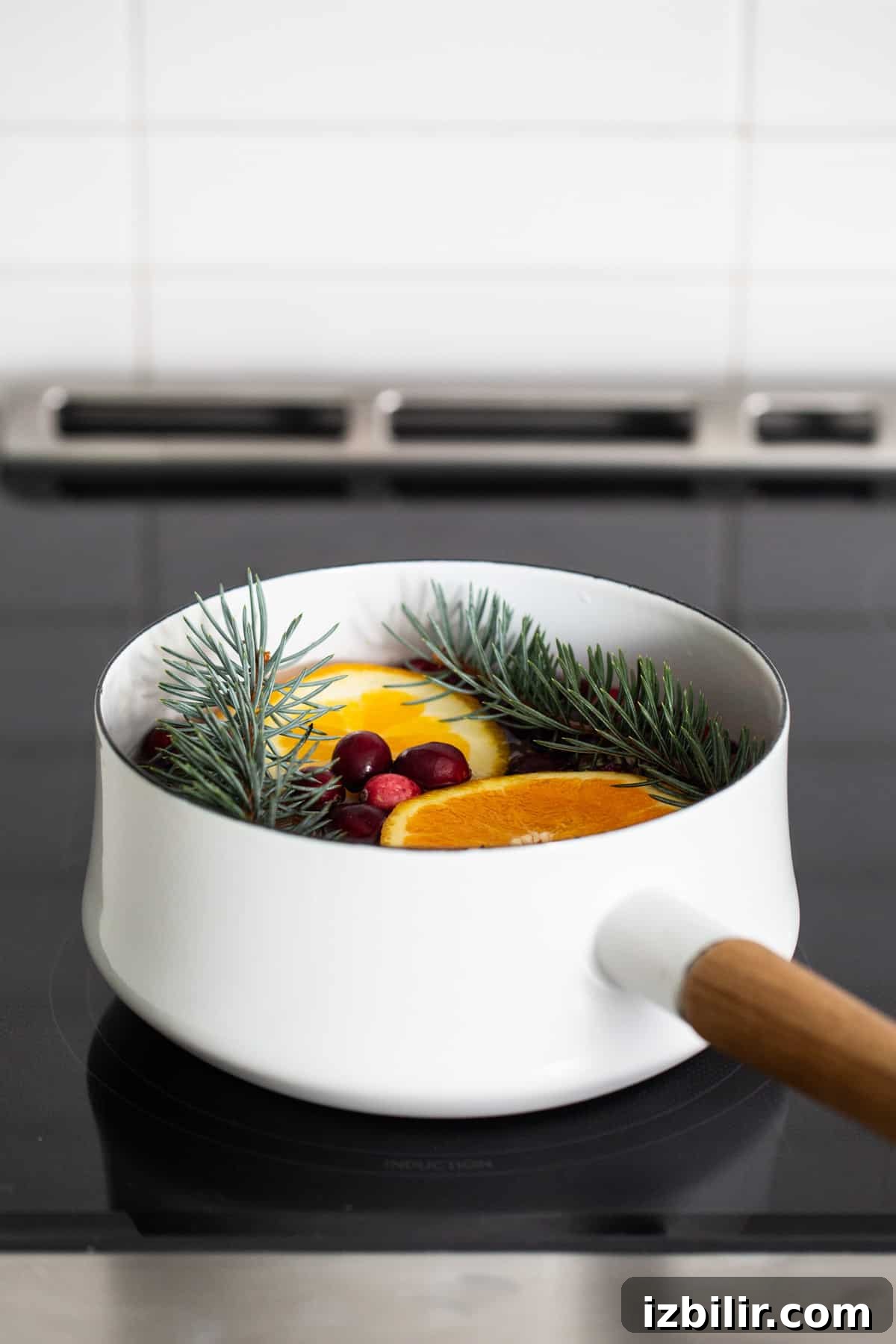 Holiday Simmer Pot Recipe for a Cozy, Fragrant Home 4 A white pan with oranges and pine needles on top of a stove.