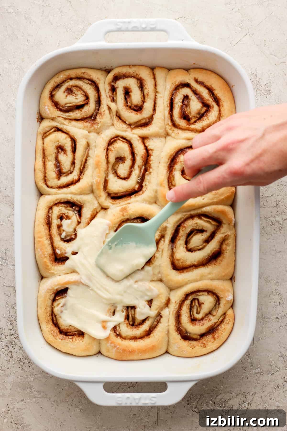 Brown Butter Banana Bread Cinnamon Rolls Recipe 5 A person dipping a spatula into a dish of cinnamon rolls.