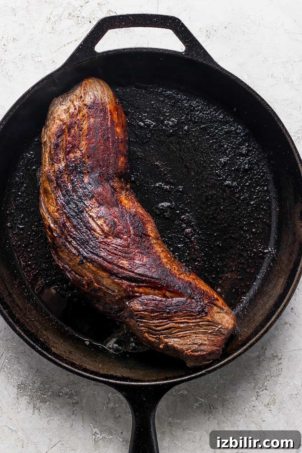 A steak is being cooked in a cast iron skillet.