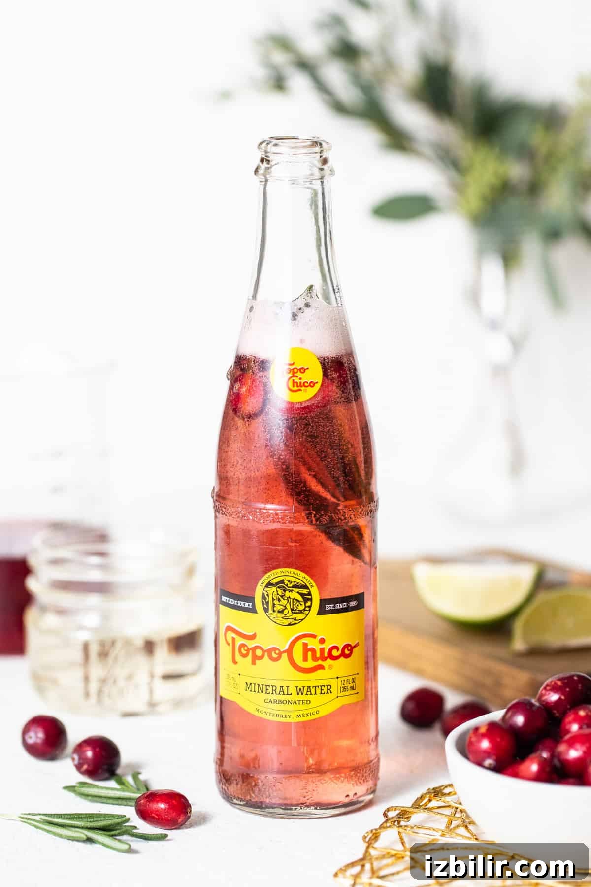 A bottle of cranberry juice with fresh cranberries and sprigs of rosemary.