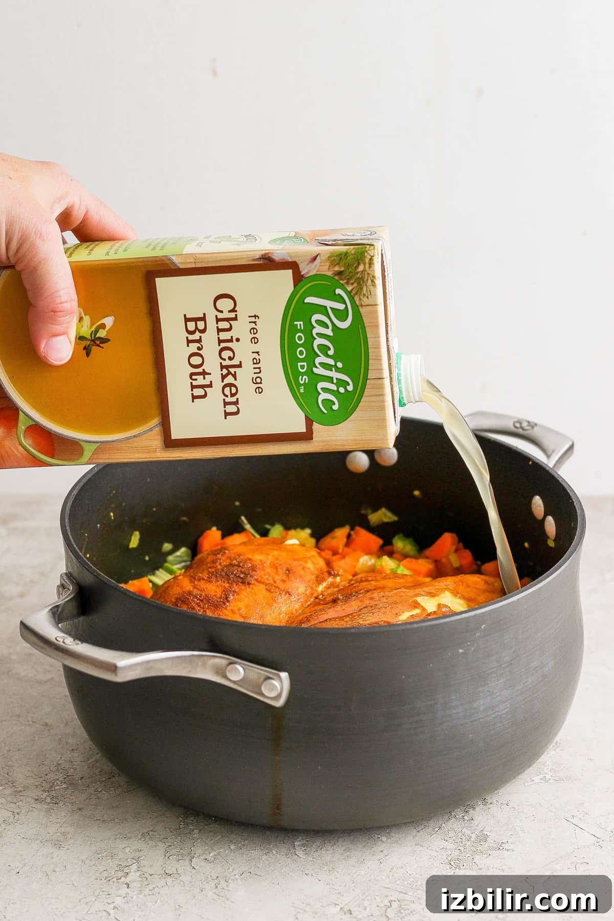 Golden Chicken and Orzo Soup Recipe 5 A person pouring a bottle of liquid into a pan.
