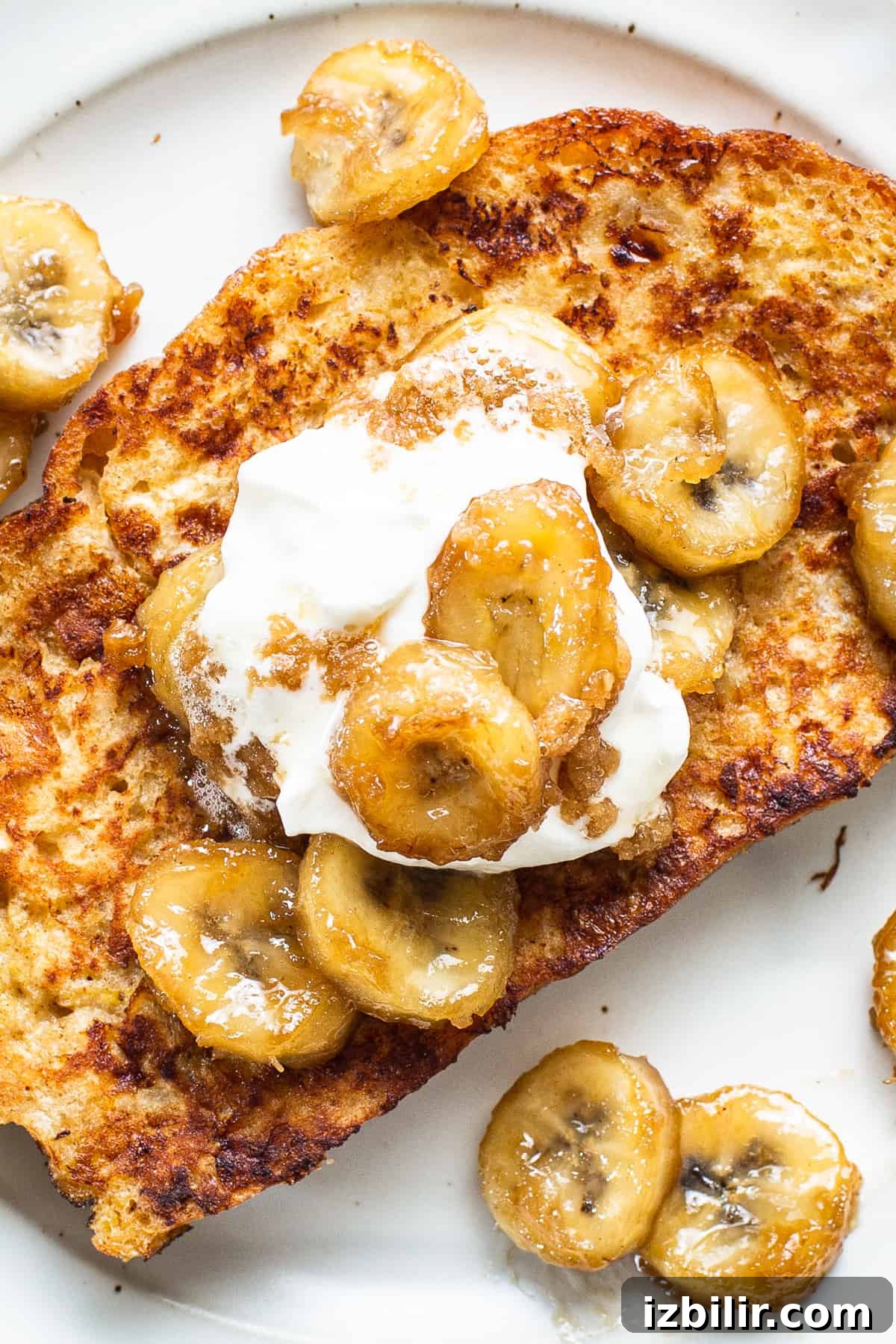 Caramelized Bananas Foster French Toast with Rum Sauce 2 A plate of french toast with banana slices and whipped cream.