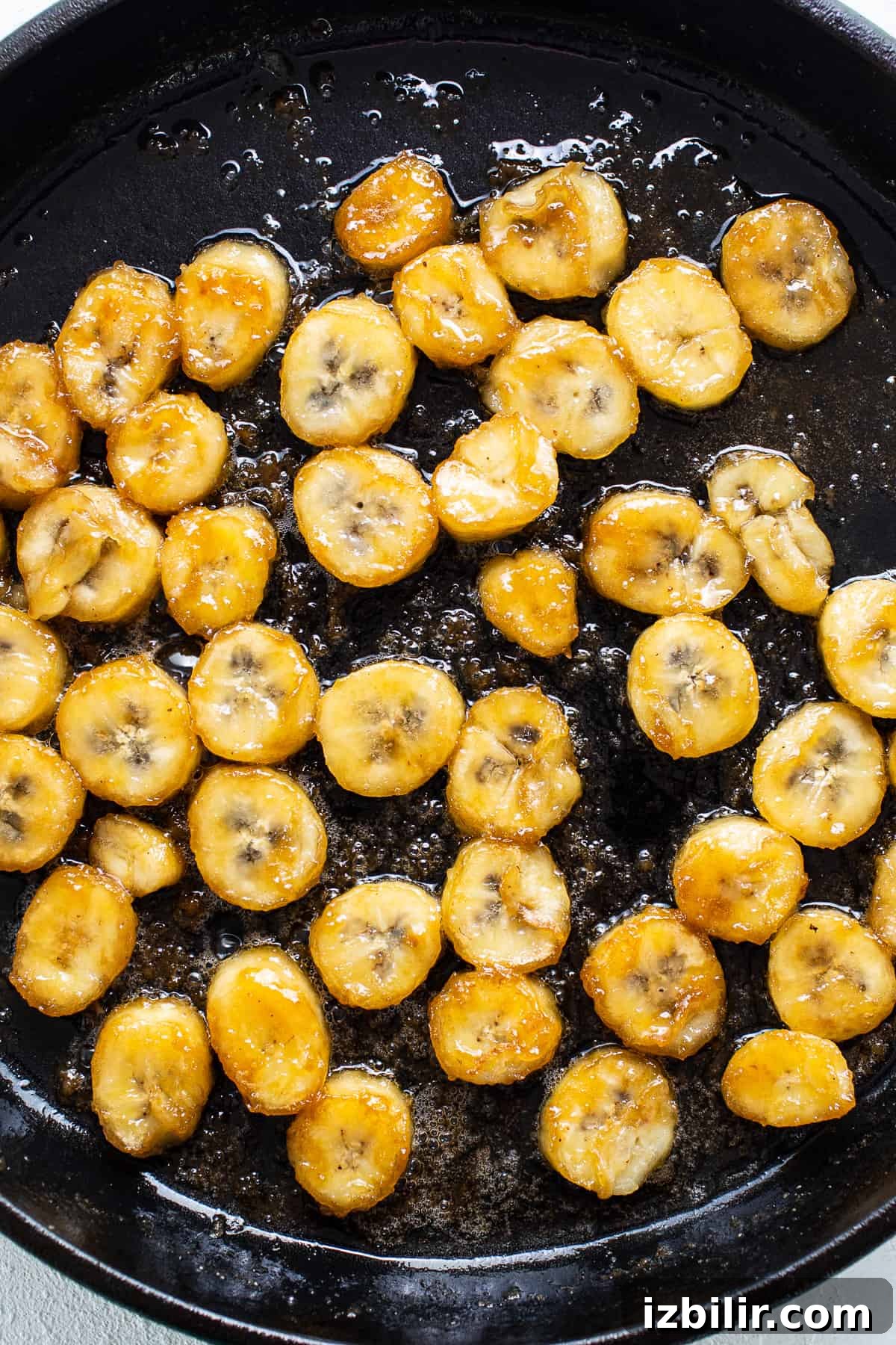 Sliced bananas are being fried in a skillet.