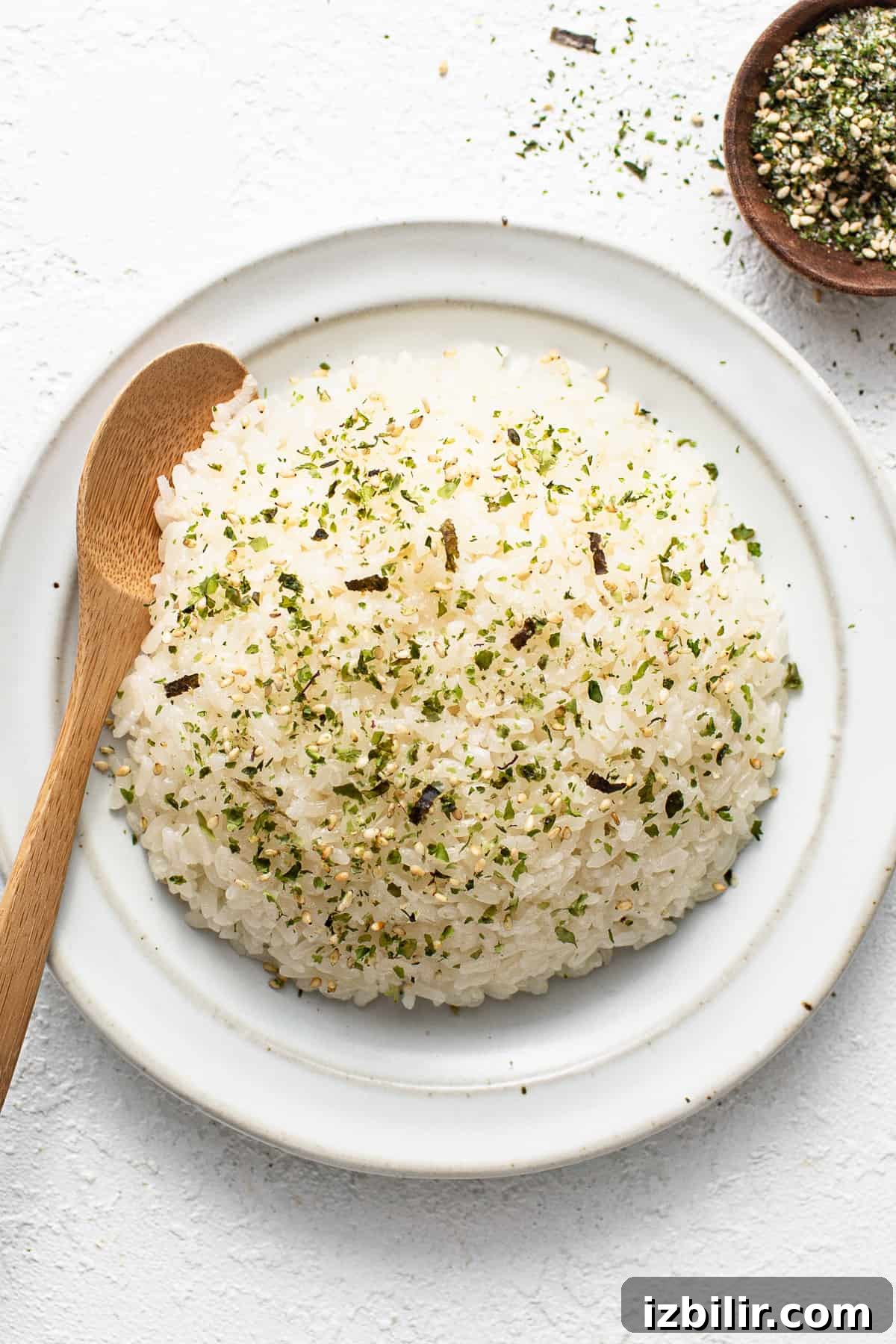 White rice on a white plate with a wooden spoon.