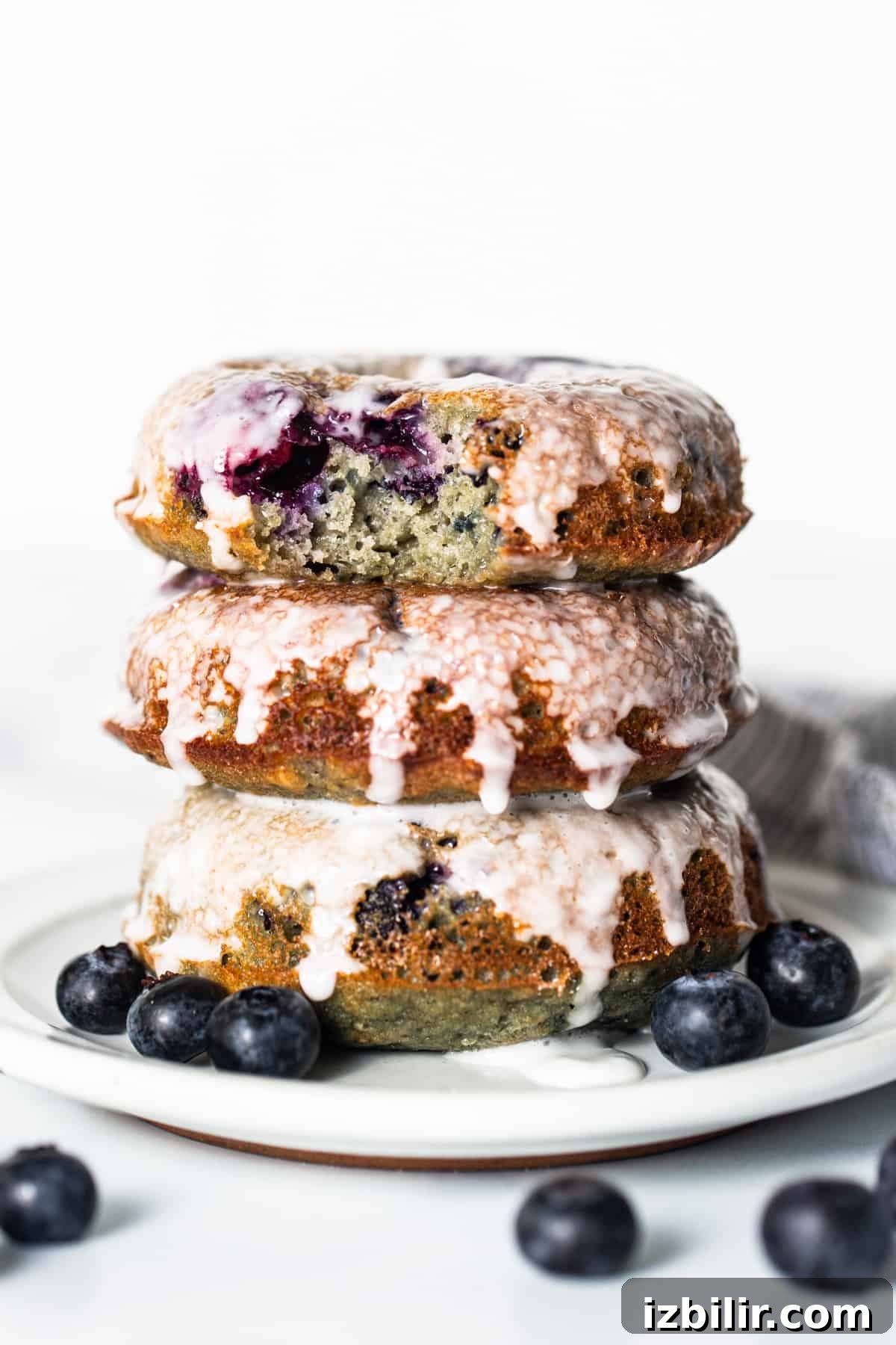 A stack of blueberry glazed donuts on a plate.