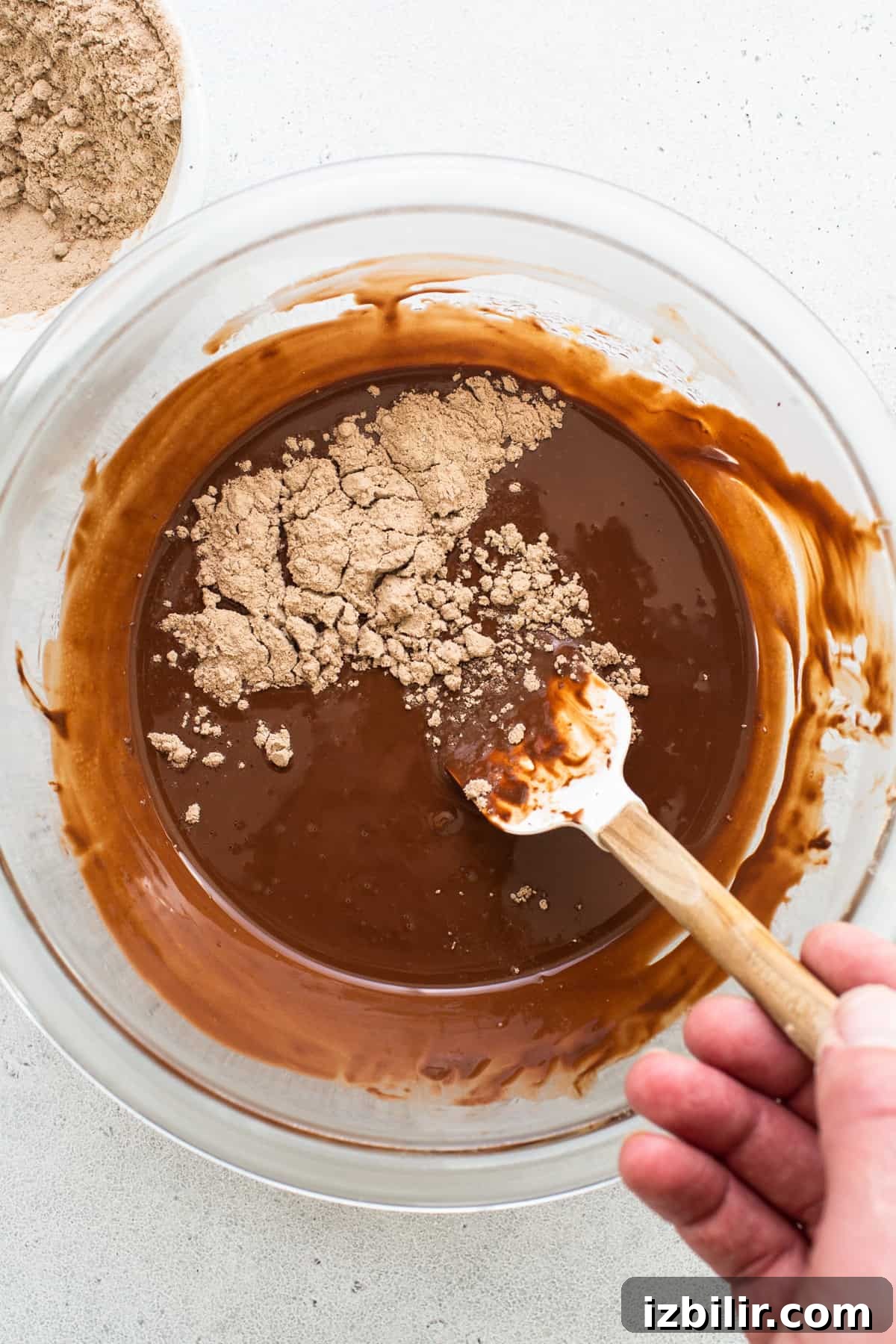 A person mixing chocolate in a bowl with a wooden spoon.