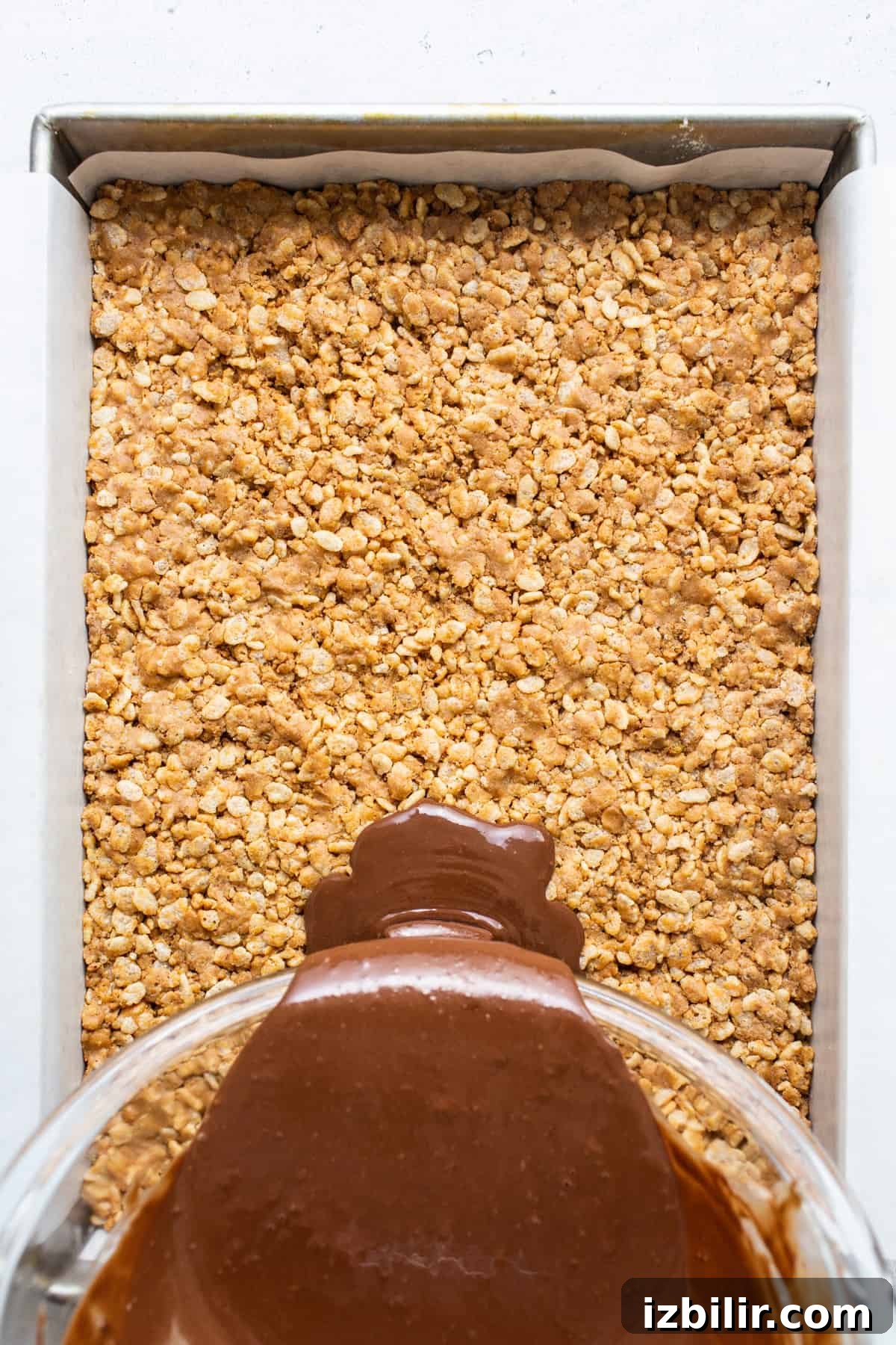 A chocolate sauce being poured over oats in a baking dish.