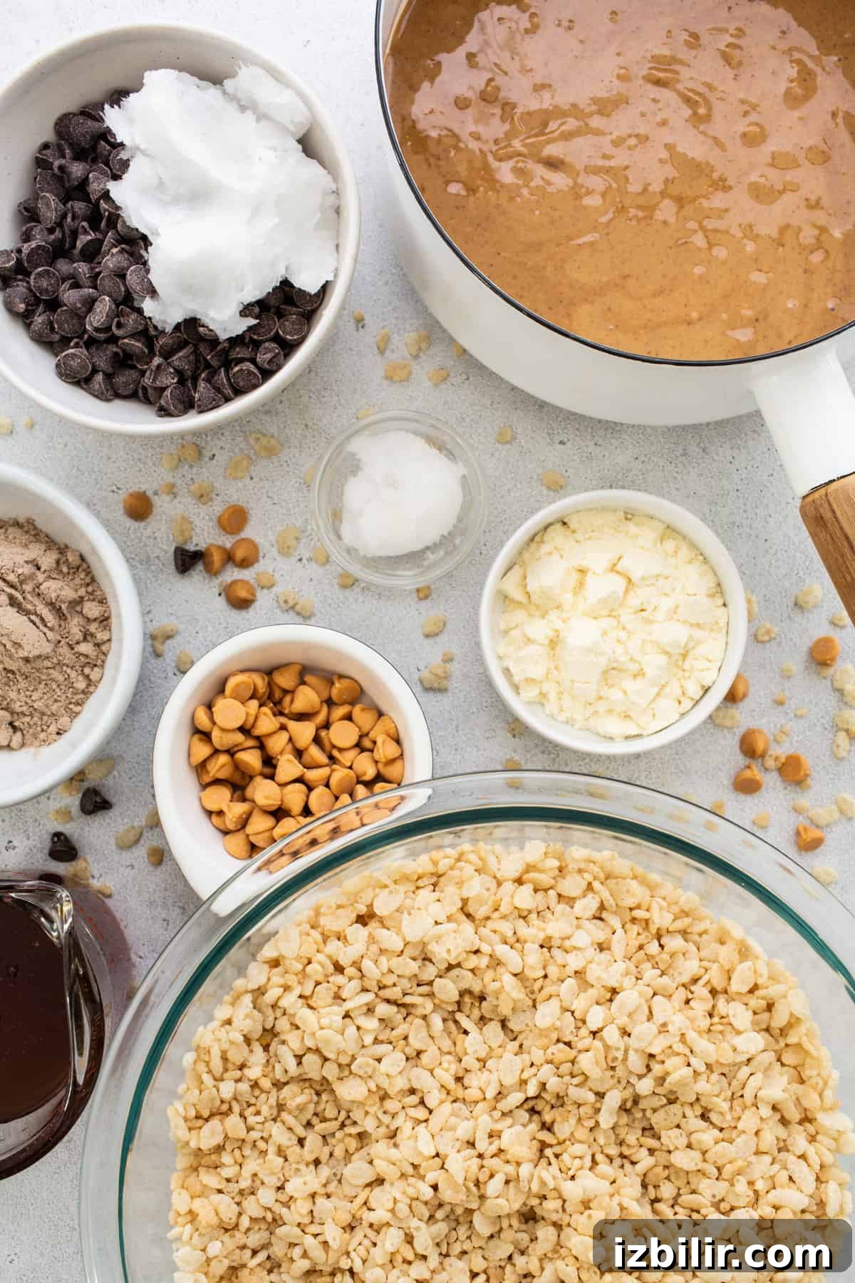 Oats, chocolate chips, peanut butter and other ingredients in bowls on a white background.