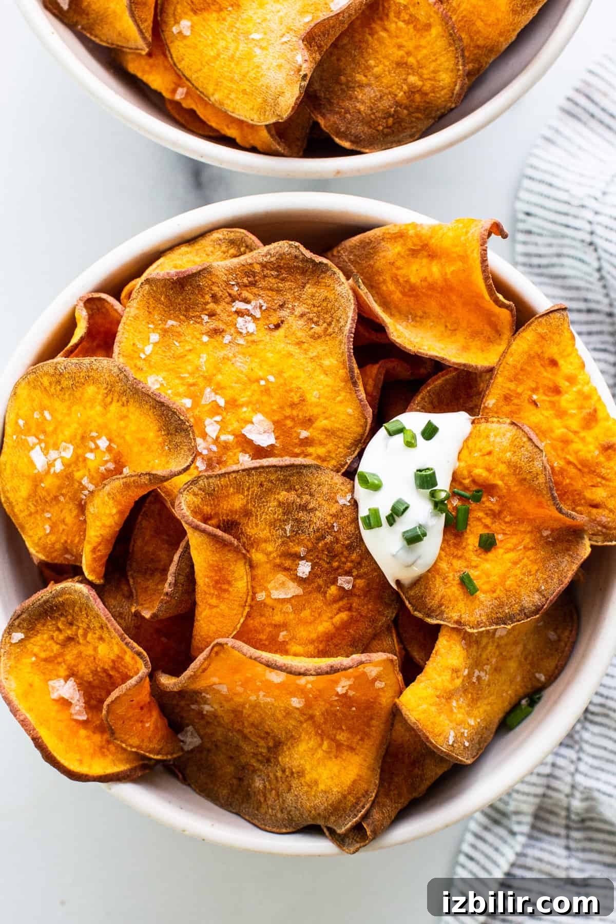 Two bowls of sweet potato chips with sour cream and chives.