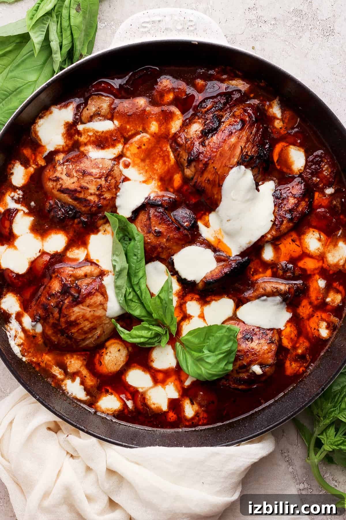 Sticky Balsamic Chicken Thighs with Garlic 2 A skillet with chicken in a sauce with basil leaves.