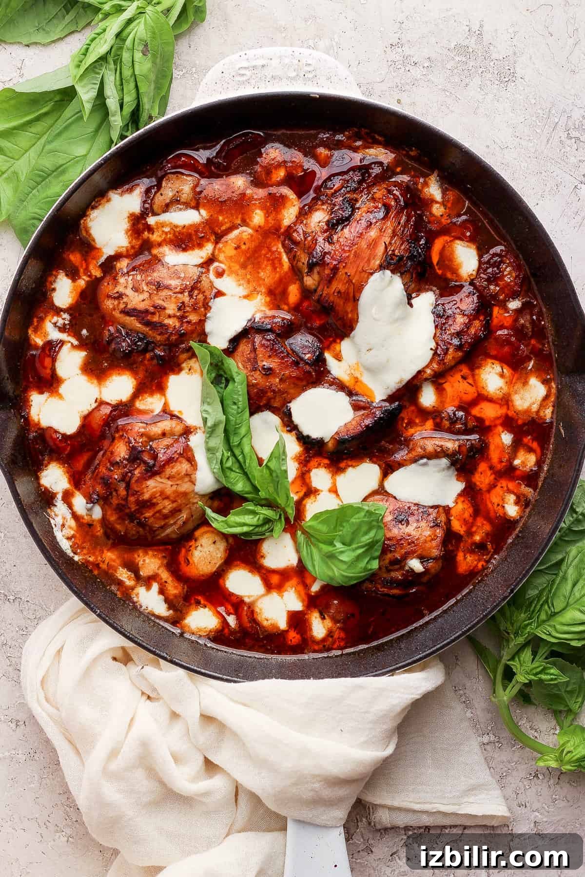 Sticky Balsamic Chicken Thighs with Garlic 7 A skillet with chicken in a sauce with basil leaves.