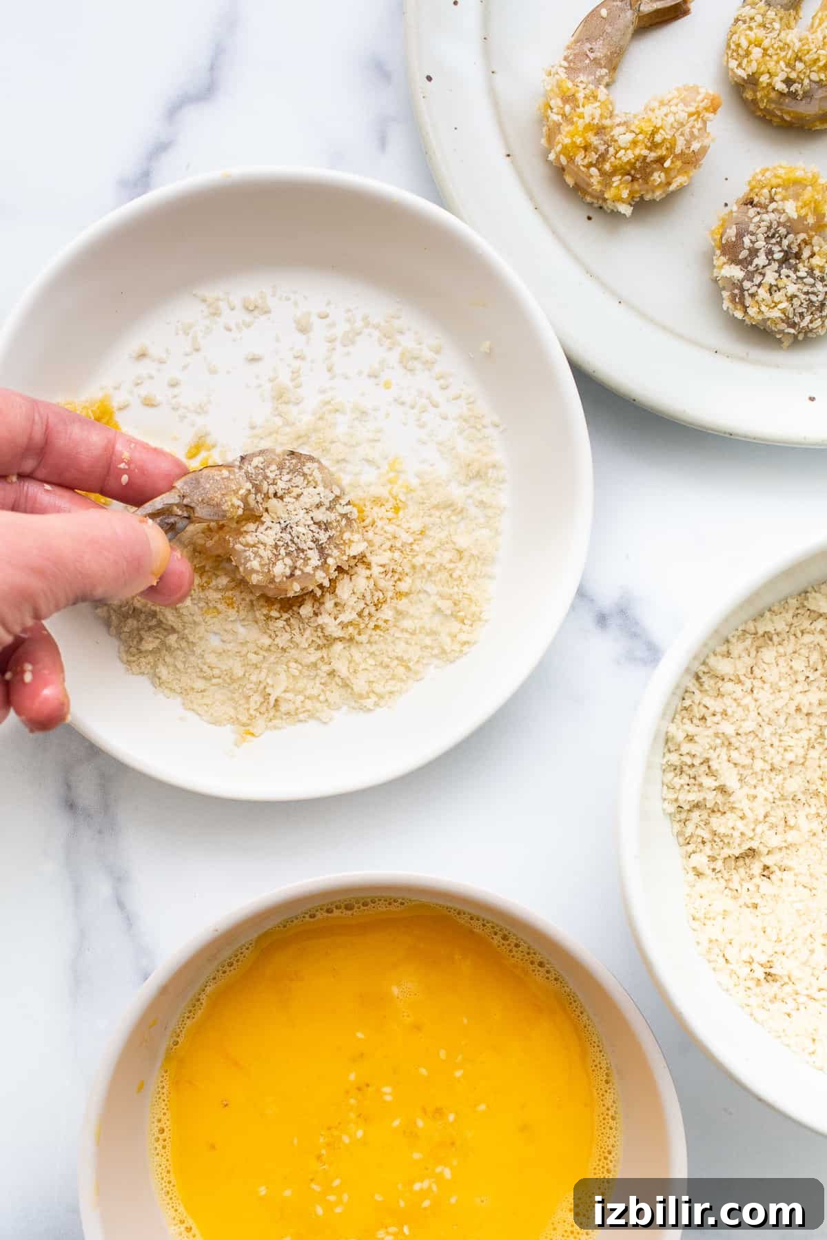 A person drizzling sesame seeds into a bowl of ingredients.