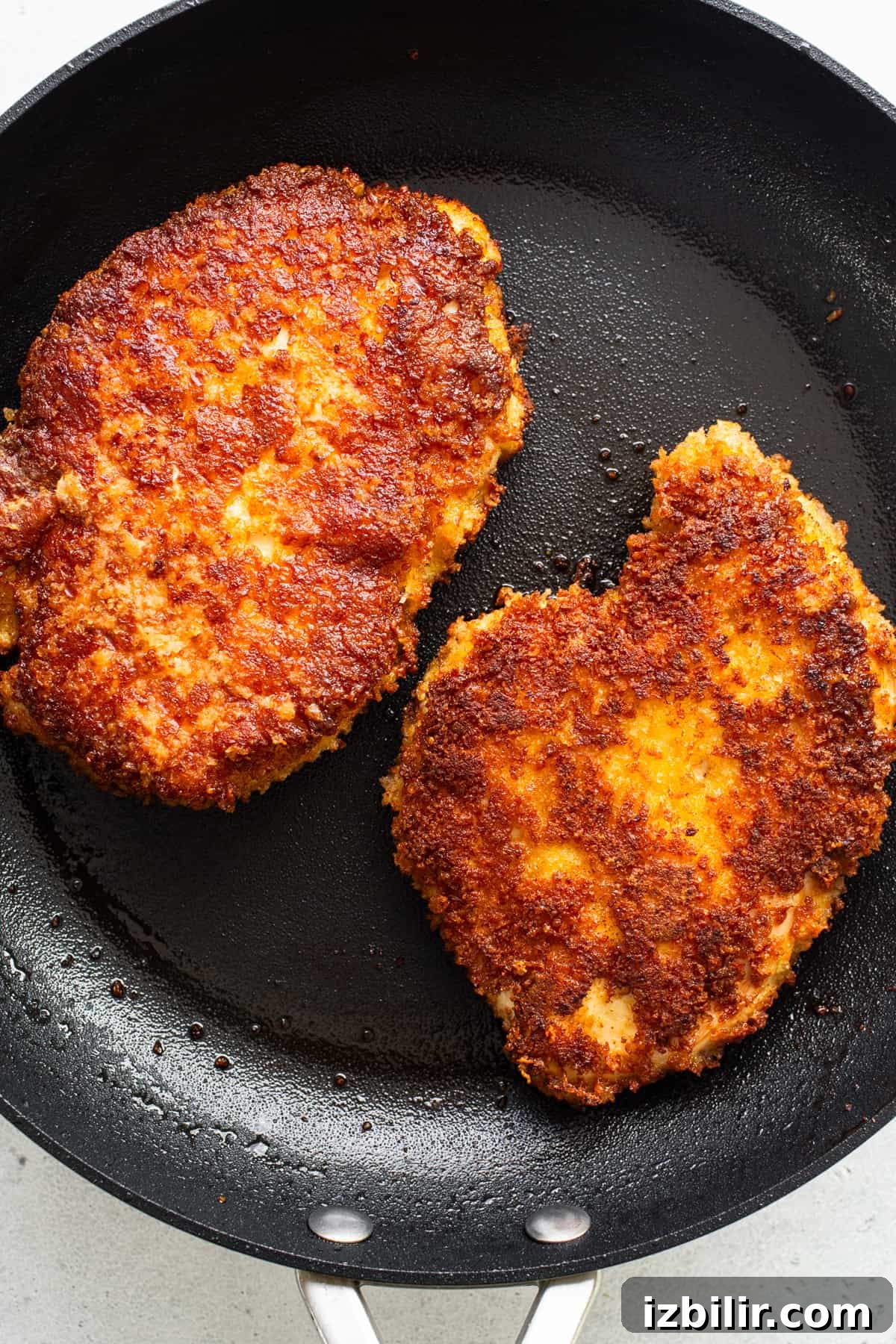 Two fried chicken patties in a frying pan.