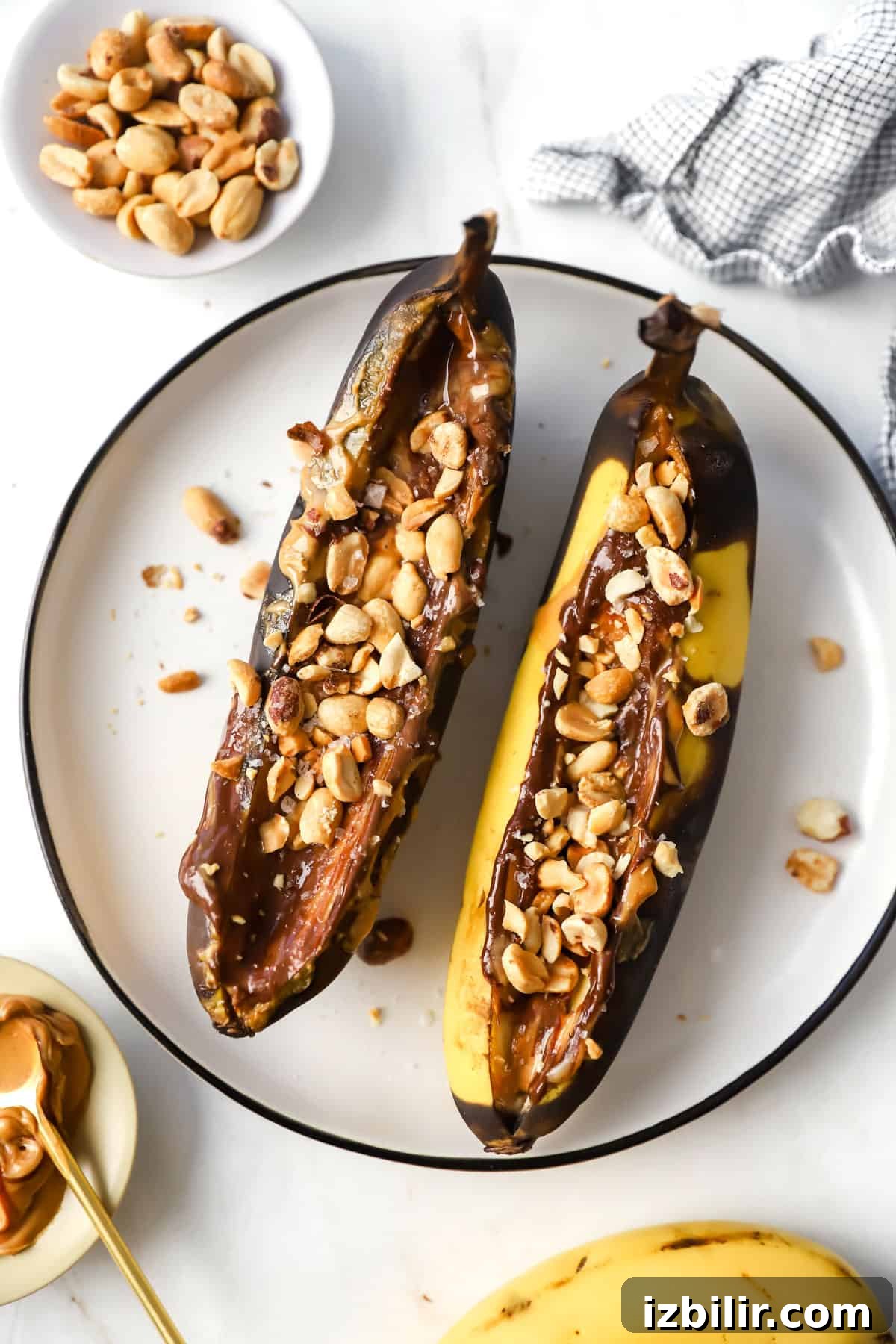 Air Fryer Banana Split with Caramel and Toasted Nuts 2 Two bananas with peanut butter and nuts on a plate.
