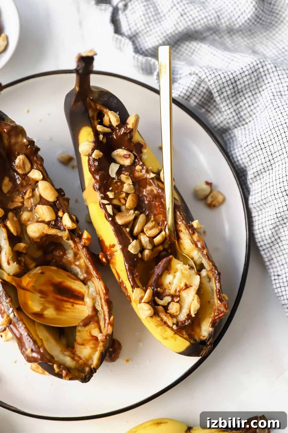 Air Fryer Banana Split with Caramel and Toasted Nuts 4 Two stuffed bananas on a plate with nuts.