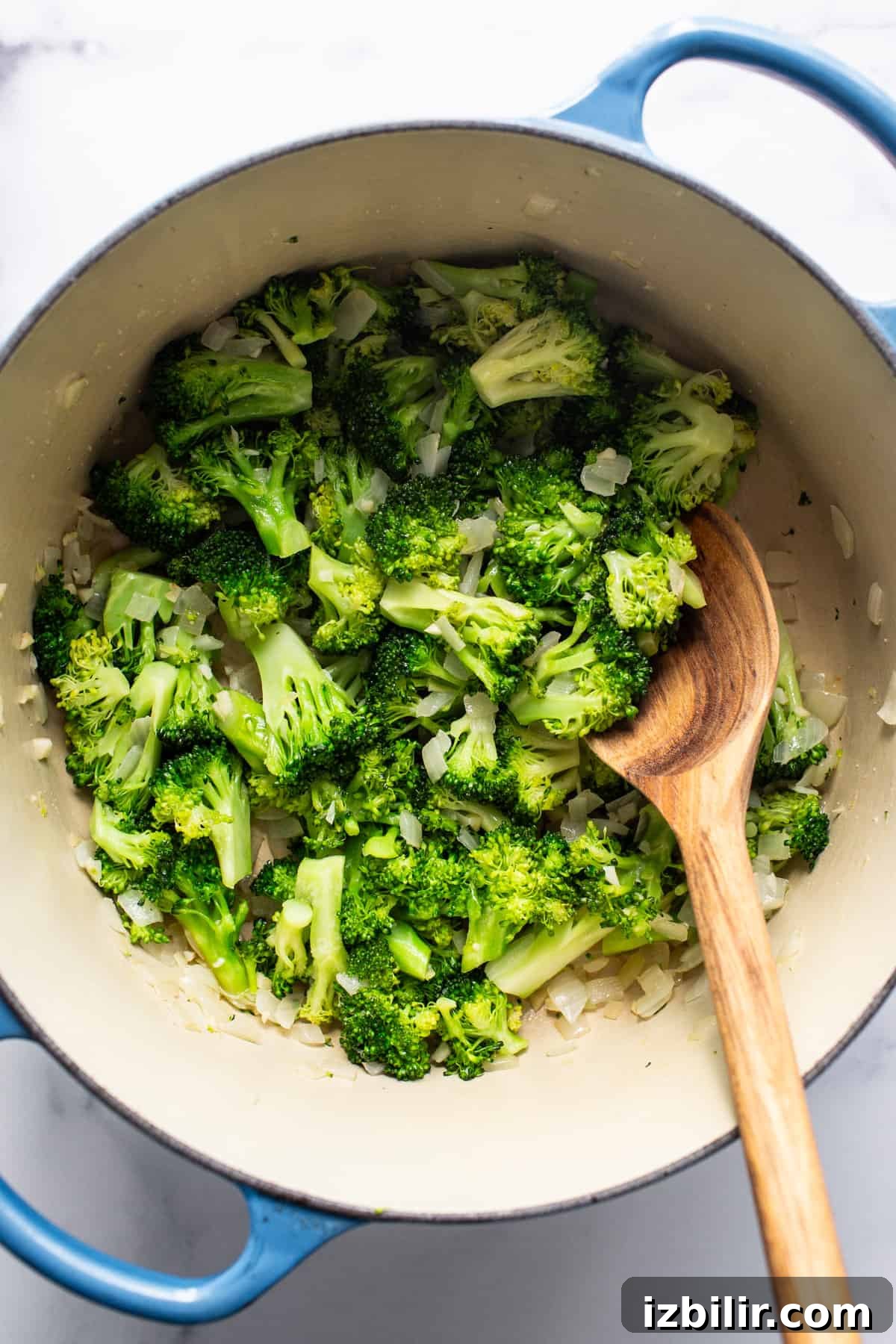 Broccoli in a blue pot with a wooden spoon.