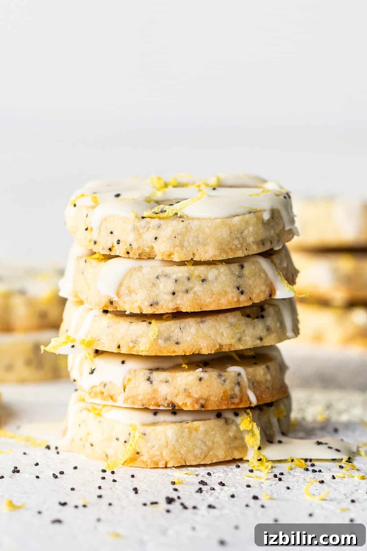 Zesty Lemon Poppy Seed Shortbread Cookies Recipe 2 A stack of cookies with white frosting.