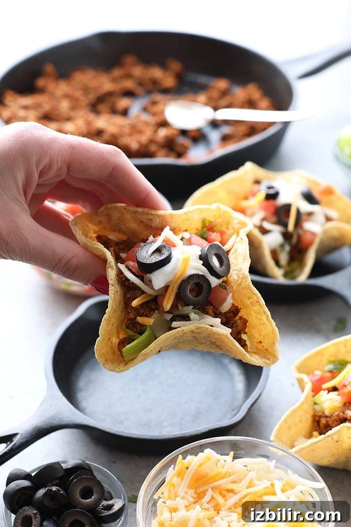 Taco night just got a whole lot cuter! Get the whole family involved and make these adorable mini taco cups made with homemade hard shell taco boats. A hand holding a mini taco cup.