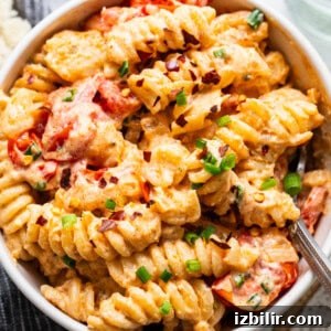 A bowl of creamy pasta with tomato pieces and sprinkled with herbs.