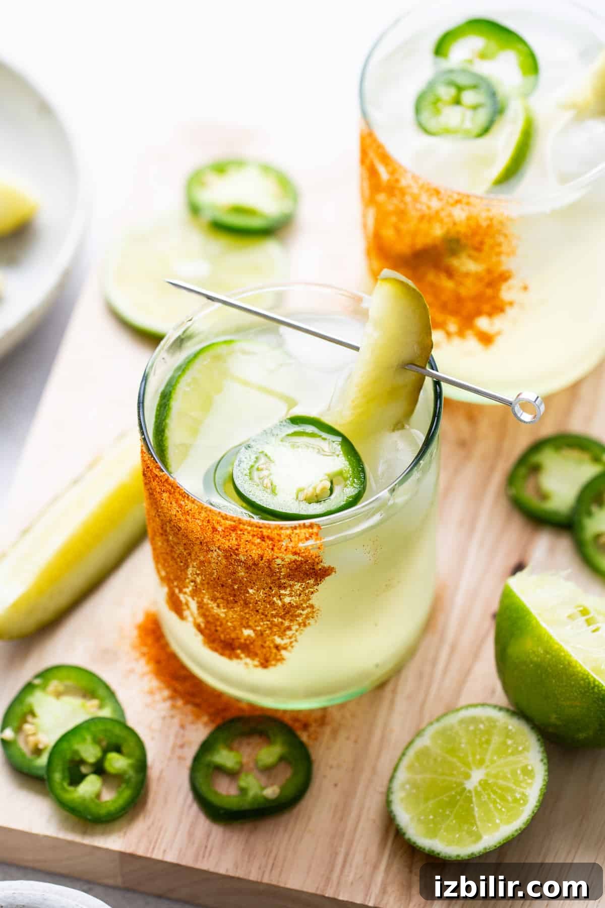 A spicy pickle margarita in a glass with pickle slices and lime wedges.