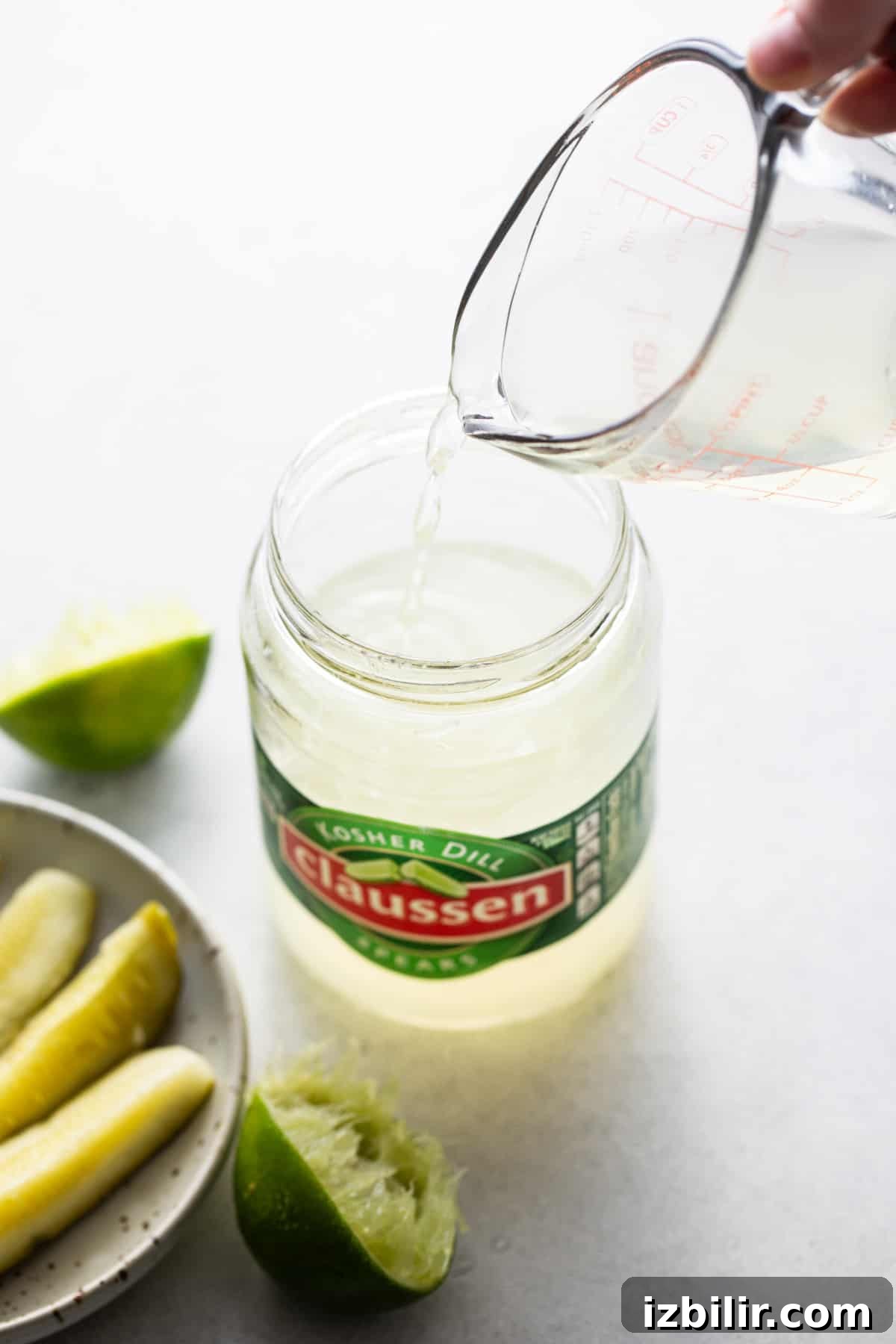 Pouring pickle juice into a cocktail shaker for a spicy pickle margarita.