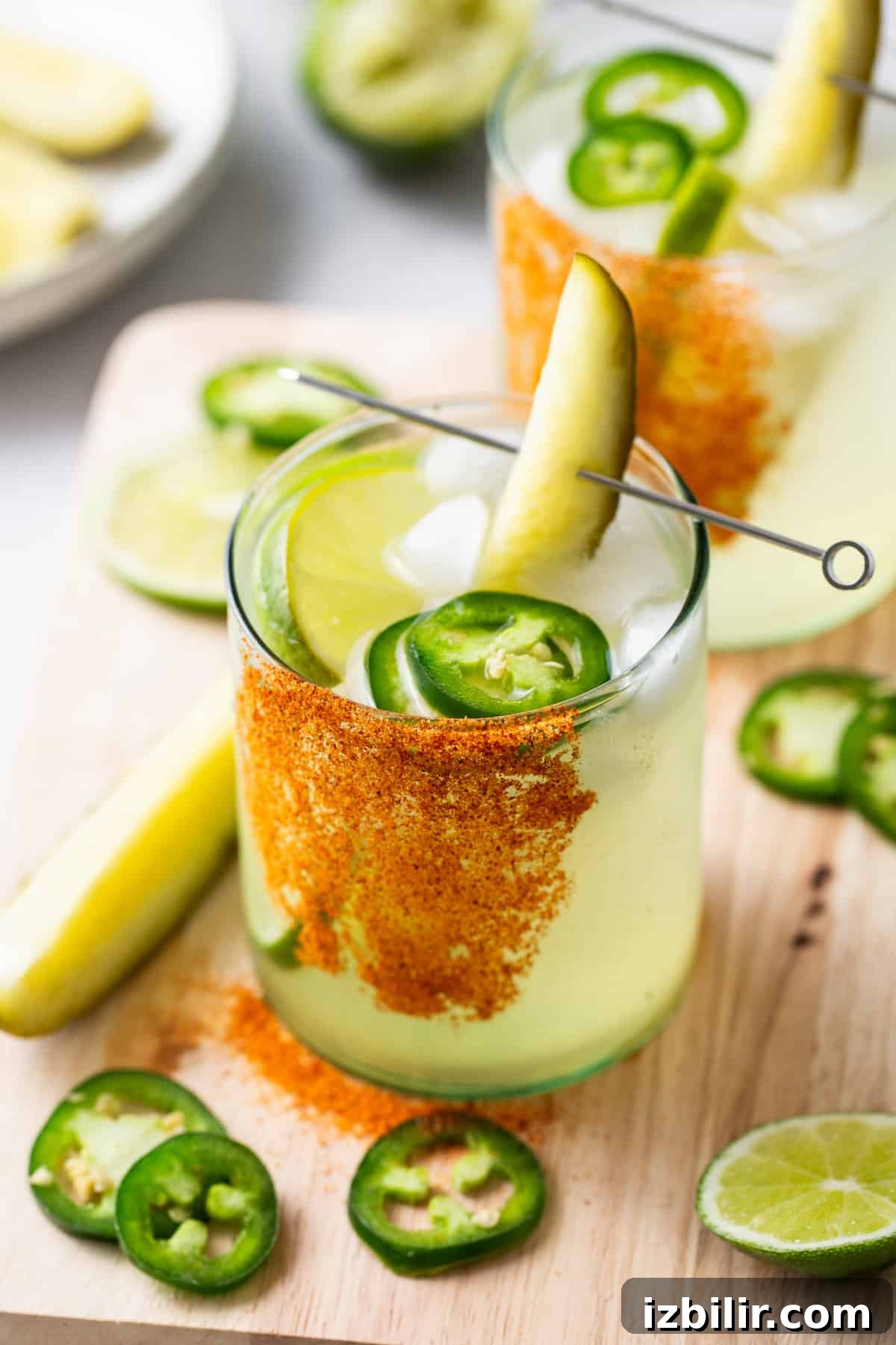 Two spicy pickle margaritas garnished with jalapeño and lime.