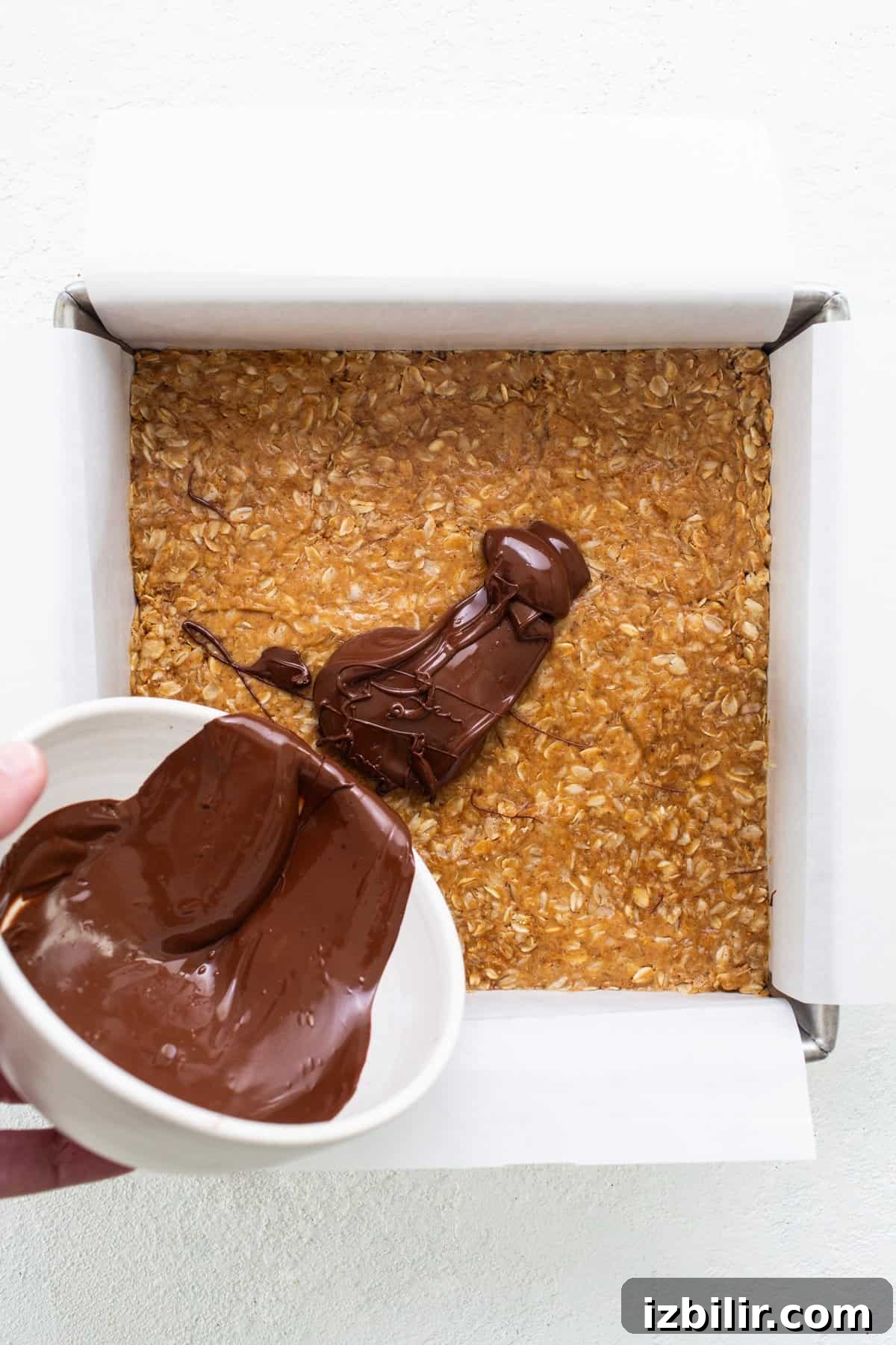 A person pouring chocolate into a box of oats.